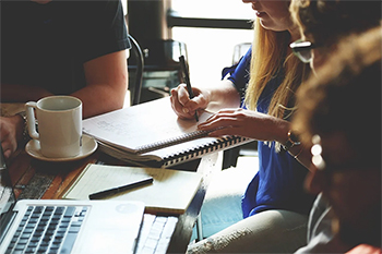 Group of people surrounding a coffee table, with notebooks, Laptop on table